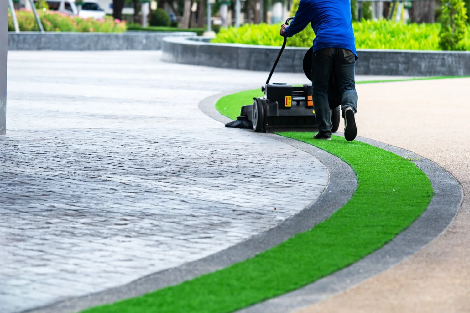 Grounds maintenance worker using a turf sweeper along a landscaped walkway