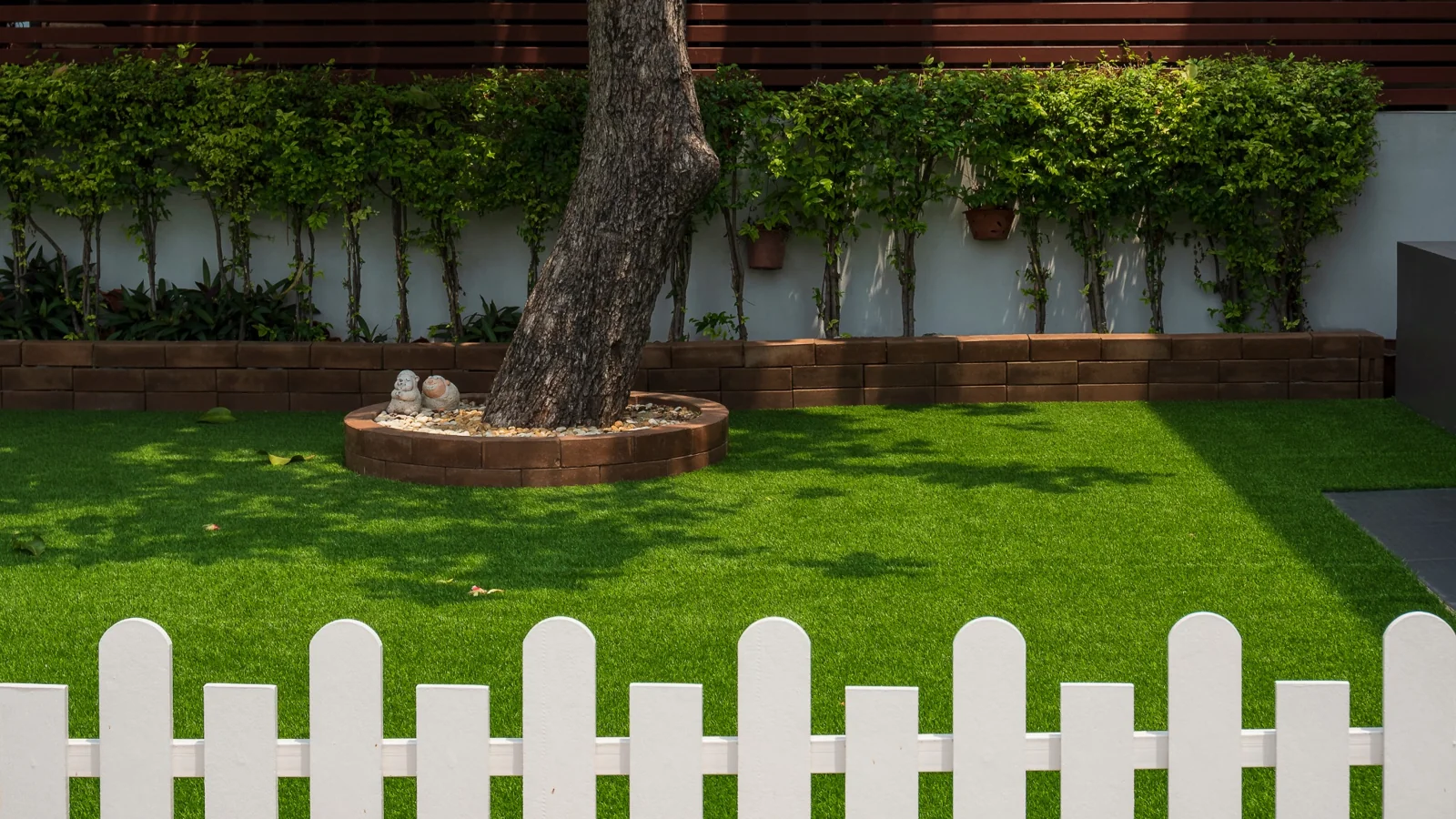 Clean green residential artificial turf yard with garden and white fence